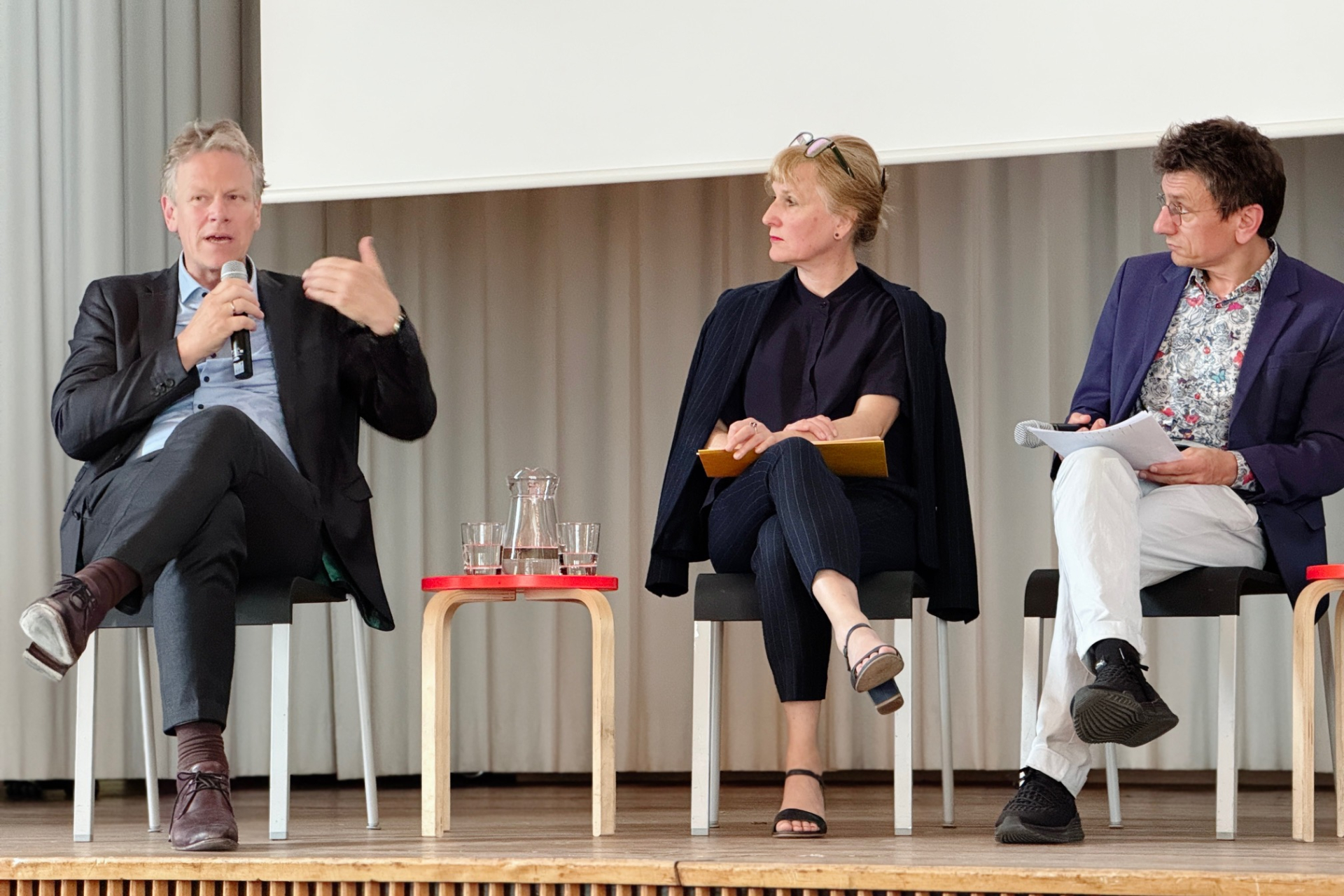 Das Foto zeigt Frank Bösch mit Mikrofon in der HAnd (links) auf dem Podium in der Aula der KHB am 4.6.2026. 