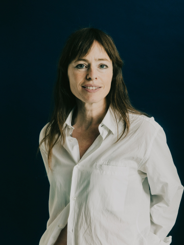 Hedwig Richter. Sie trägt eine weiße Bluse und steht vor einem dunklen Hintergrund. 