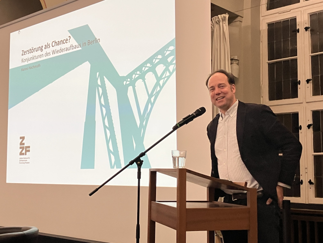 Das Foto zeigt den Historiker bei einem Vortrag 2025 am Pult, links neben ihm sieht man das groß das Logo des ZZF Potsdam.