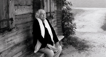 Das Foto zeigt Thomas Harlan auf einer Bank vor einer Blockhütte sitzend im Berchtesgadener Land