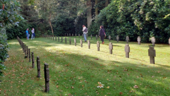 Das Bild zeigt einen Blick auf die dänische Kriegsgräberstätte Oksbø, zu sehen sind drei Reihen von Kreuzen und am Ende des Fotos vier Personen.