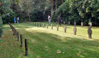 Das Bild zeigt einen Blick auf die dänische Kriegsgräberstätte Oksbø, zu sehen sind drei Reihen von Kreuzen und am Ende des Fotos vier Personen.