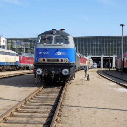 Eine blau lackierte Lokomotive steht vor einem Betriebsgebäude in Neustrelitz.