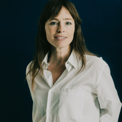 Hedwig Richter. Sie trägt eine weiße Bluse und steht vor einem dunklen Hintergrund. 